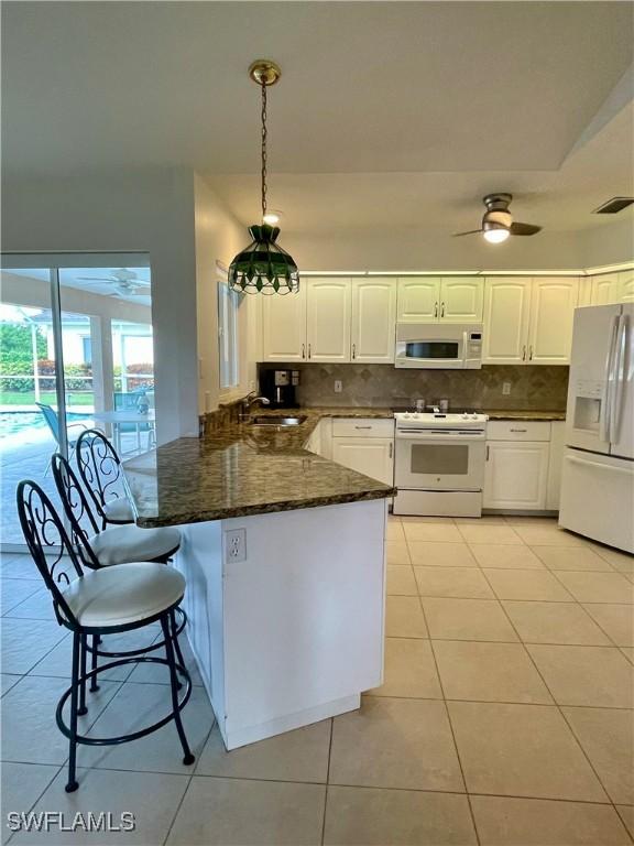 86 Pinehurst Pl, Rotonda West, FL 33947 - kitchen featuring white appliances, light tile patterned floors, ceiling fan, white cabinets, and tasteful backsplash