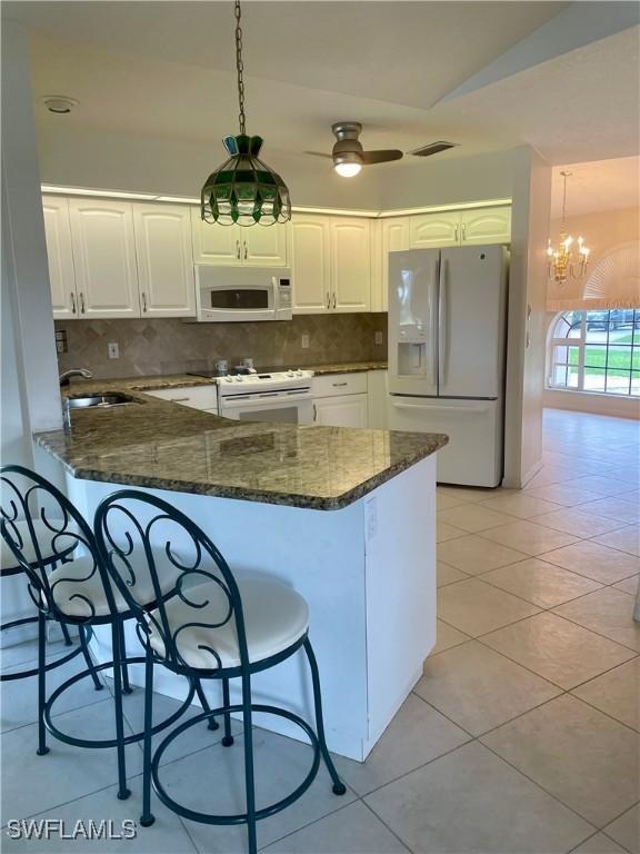 86 Pinehurst Pl, Rotonda West, FL 33947 - kitchen featuring white appliances, a kitchen bar, a peninsula, and white cabinets