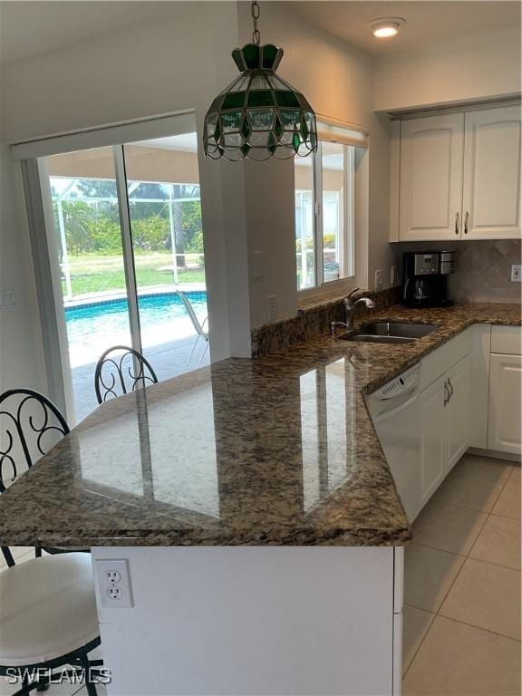 86 Pinehurst Pl, Rotonda West, FL 33947 - kitchen with dishwasher, a peninsula, dark stone countertops, white cabinets, and light tile patterned floors