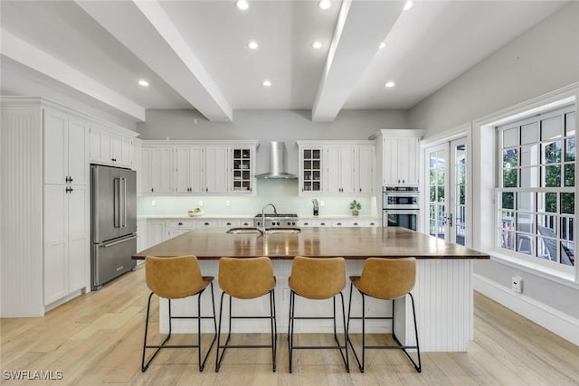 1550 Gordon Dr, Naples, FL 34102 - kitchen with appliances with stainless steel finishes, wall chimney range hood, beamed ceiling, a sink, and light wood-style floors