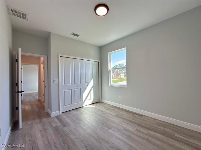 unfurnished bedroom with wood finished floors, baseboards, and a closet