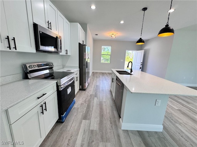 kitchen featuring appliances with stainless steel finishes, a sink, light wood-type flooring, an island with sink, and white cabinetry