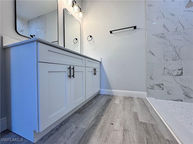 bathroom featuring wood finished floors, vanity, baseboards, and tiled shower