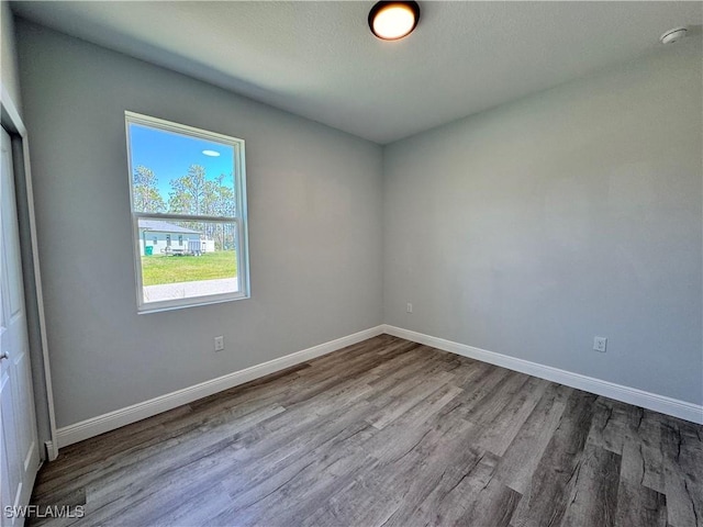 empty room with wood finished floors, baseboards, and a smoke detector