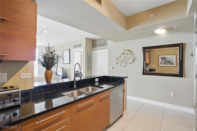 kitchen with a sink, stainless steel dishwasher, light tile patterned floors, dark stone countertops, and baseboards