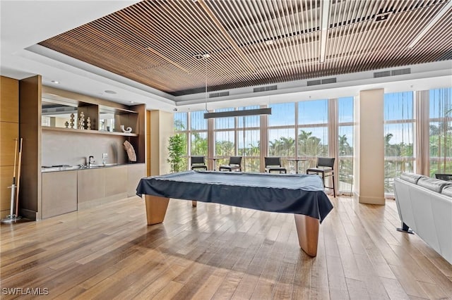 playroom featuring billiards table, light wood-type flooring, a raised ceiling, healthy amount of natural light, and floor to ceiling windows