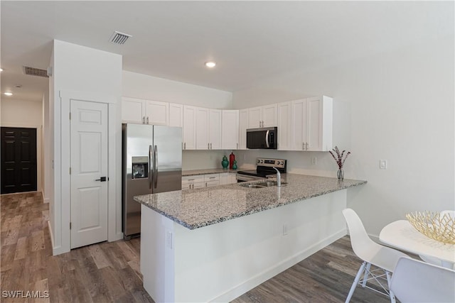 5205/5207 26th St SW, Lehigh Acres, FL 33973 - kitchen featuring appliances with stainless steel finishes, a peninsula, wood finished floors, white cabinets, and light stone countertops