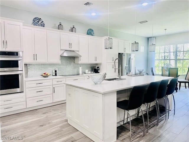5489 Whispering Willow Way, Fort Myers, FL 33908 - kitchen featuring appliances with stainless steel finishes, a sink, under cabinet range hood, a kitchen breakfast bar, and white cabinets