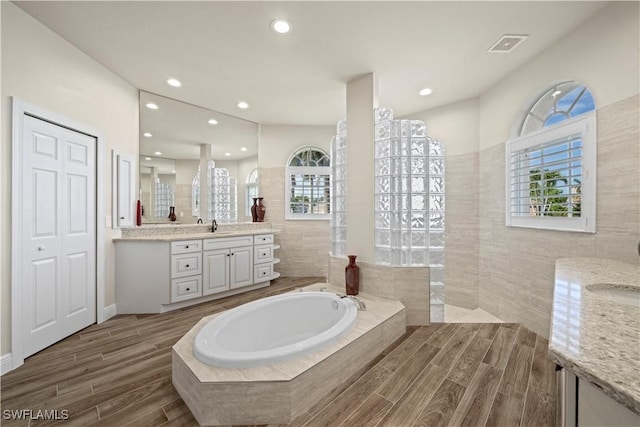 1069 SW 57th St, Cape Coral, FL 33914 - full bathroom featuring vanity, a garden tub, wood finished floors, plenty of natural light, and tile walls