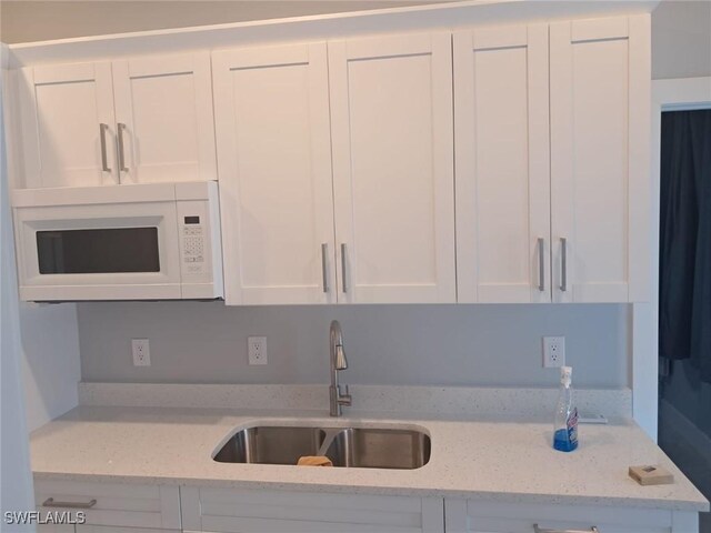 3016 6th St W, Lehigh Acres, FL 33971 - kitchen featuring a sink, white microwave, white cabinetry, and light stone counters