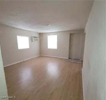 unfurnished room with an AC wall unit, light wood-style floors, and baseboards