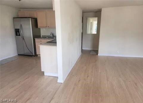 kitchen featuring stainless steel refrigerator with ice dispenser, light wood-type flooring, and baseboards