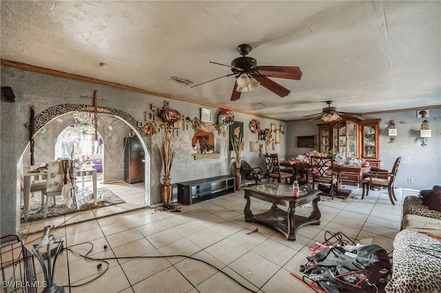 living area featuring a ceiling fan, crown molding, light tile patterned floors, arched walkways, and a fireplace