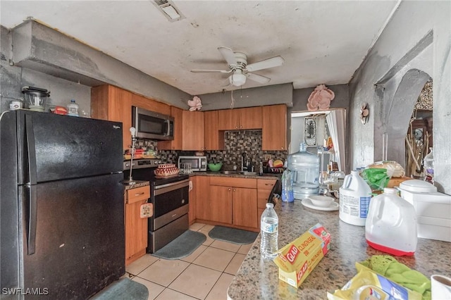 kitchen featuring stainless steel appliances, a sink, backsplash, ceiling fan, and brown cabinetry