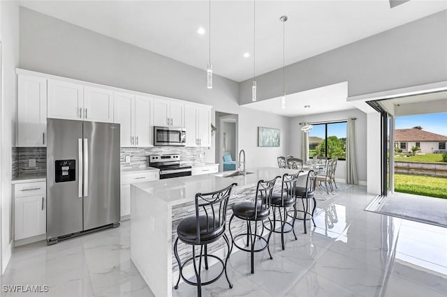 1409 SW 24th St, Cape Coral, FL 33991 - kitchen with stainless steel appliances, decorative backsplash, light marble finish floors, white cabinets, and a large island with sink
