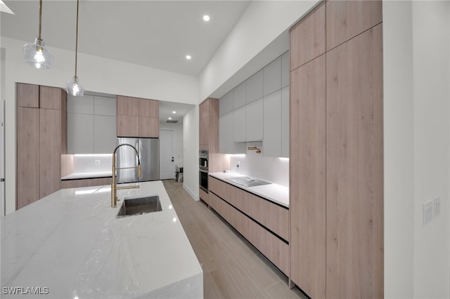 419 NW 7th Ave, Cape Coral, FL 33993 - kitchen with modern cabinets, a sink, light stone countertops, light wood-type flooring, and hanging light fixtures