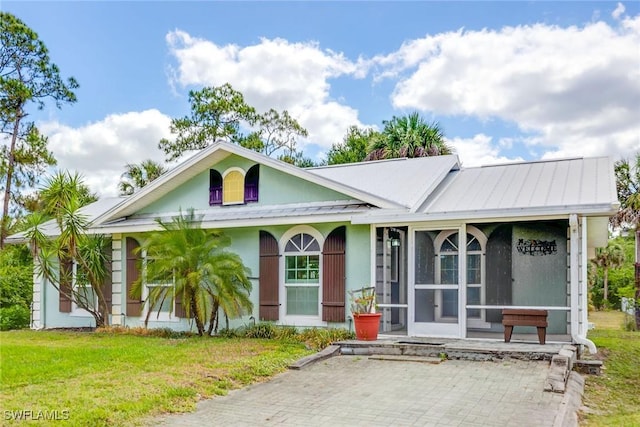 180 20th St SE, Naples, FL 34117 - view of front of home with a sunroom, metal roof, a standing seam roof, a front yard, and stucco siding