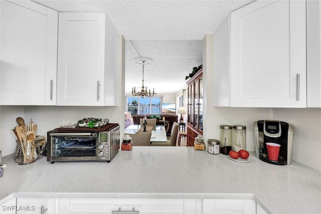 1829 SE 41st St Unit 1I, Cape Coral, FL 33904 - kitchen with a textured ceiling, white cabinetry, a chandelier, and light stone counters