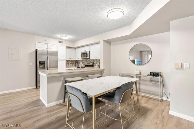1150 Wildwood Lakes Blvd Unit 203, Naples, FL 34104 - kitchen featuring stainless steel appliances, a peninsula, a textured ceiling, white cabinets, and light wood-type flooring