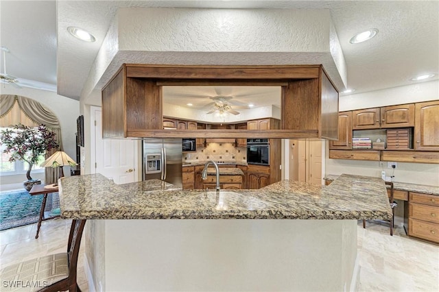 414 Caicos Dr, Punta Gorda, FL 33950 - kitchen with stainless steel fridge, oven, a ceiling fan, brown cabinetry, and stone counters