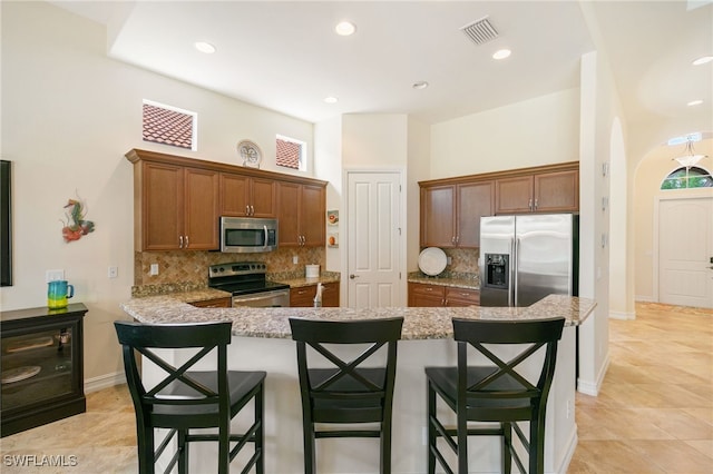 6492 Caldecott Dr, Naples, FL 34113 - kitchen featuring appliances with stainless steel finishes, a kitchen bar, backsplash, light stone countertops, and arched walkways
