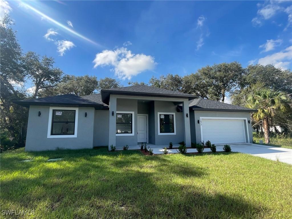 7028 Tide Cir, Labelle, FL 33935 - view of front facade with stucco siding, concrete driveway, an attached garage, a front lawn, and roof with shingles