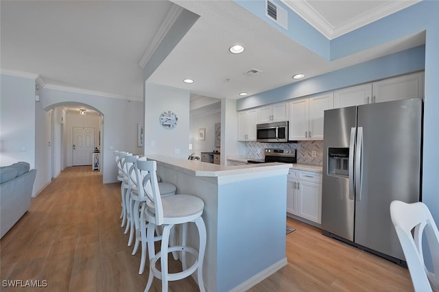 10275 Heritage Bay Blvd Unit 737, Naples, FL 34120 - kitchen featuring appliances with stainless steel finishes, arched walkways, ornamental molding, white cabinetry, and a kitchen breakfast bar