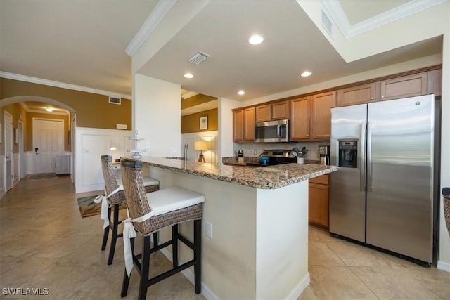 9731 Acqua Ct Unit 537, Naples, FL 34113 - kitchen featuring appliances with stainless steel finishes, arched walkways, brown cabinets, a breakfast bar, and light stone countertops
