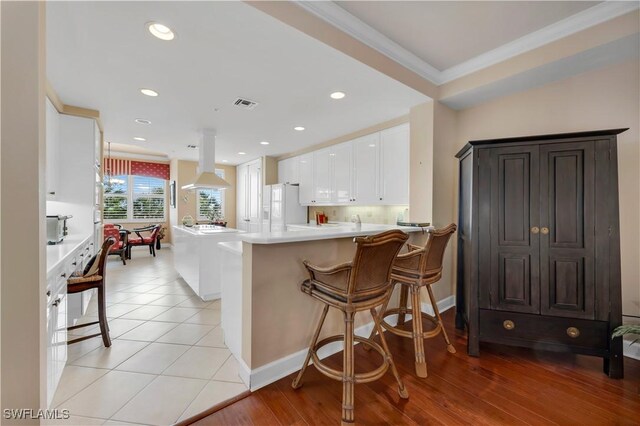 11640 Court Of Palms Unit 103, Fort Myers, FL 33908 - kitchen with island exhaust hood, white refrigerator with ice dispenser, white cabinetry, ornamental molding, and light countertops