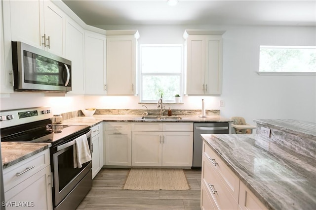 12083 Maiden Ln, Bonita Springs, FL 34135 - kitchen with stainless steel appliances, a sink, light stone countertops, light wood-style floors, and white cabinetry