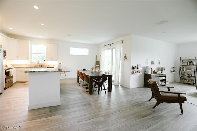 12083 Maiden Ln, Bonita Springs, FL 34135 - kitchen featuring stainless steel appliances, a sink, white cabinets, a kitchen island, and light wood finished floors