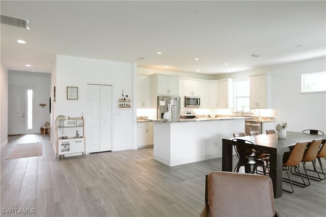 12083 Maiden Ln, Bonita Springs, FL 34135 - kitchen featuring appliances with stainless steel finishes, light wood finished floors, a center island, recessed lighting, and white cabinetry