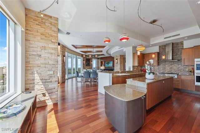 13675 Vanderbilt Dr Ph 1105, Naples, FL 34110 - kitchen featuring brown cabinets, wall chimney range hood, dark wood-type flooring, a sink, and backsplash