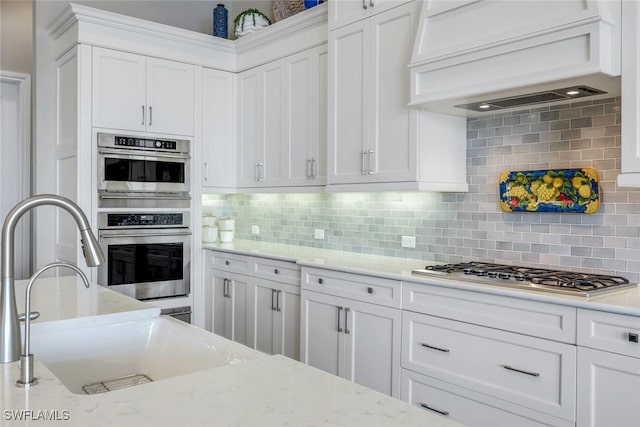 9010 Arrezo Ct, Naples, FL 34119 - kitchen with appliances with stainless steel finishes, premium range hood, white cabinetry, backsplash, and light stone counters