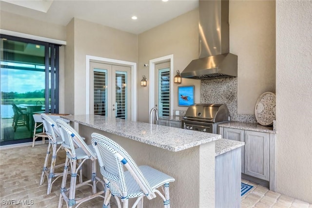 9010 Arrezo Ct, Naples, FL 34119 - kitchen with range hood, light stone counters, a kitchen breakfast bar, recessed lighting, and french doors