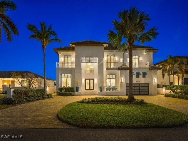 434 Conners Ave, Naples, FL 34108 - back of house at night featuring decorative driveway, a balcony, french doors, a garage, and stucco siding