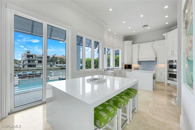 434 Conners Ave, Naples, FL 34108 - kitchen featuring a kitchen island, ornamental molding, custom exhaust hood, stainless steel double oven, and backsplash