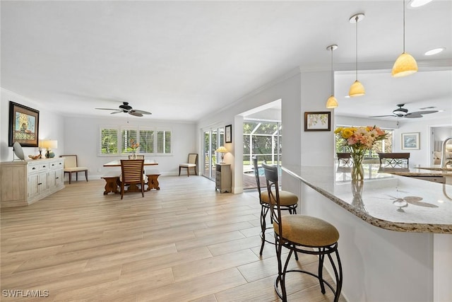 636 Park Shore Dr, Naples, FL 34103 - kitchen featuring ceiling fan, crown molding, a kitchen bar, light stone countertops, and light wood finished floors