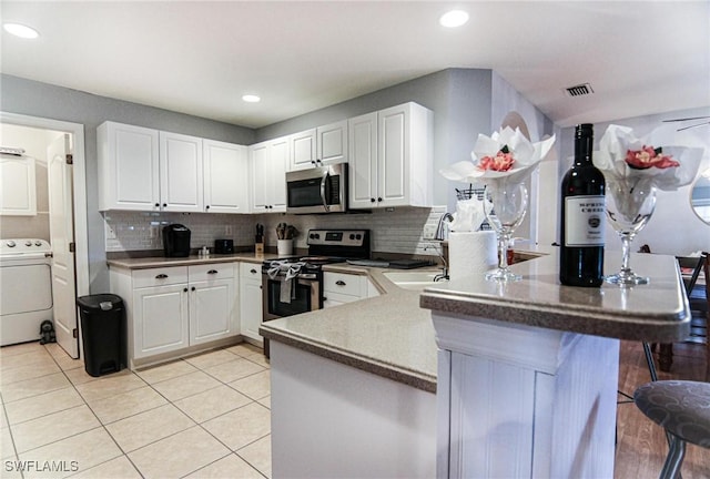 1129 NW 19th Ave, Cape Coral, FL 33993 - kitchen with washer / clothes dryer, appliances with stainless steel finishes, a peninsula, white cabinets, and decorative backsplash