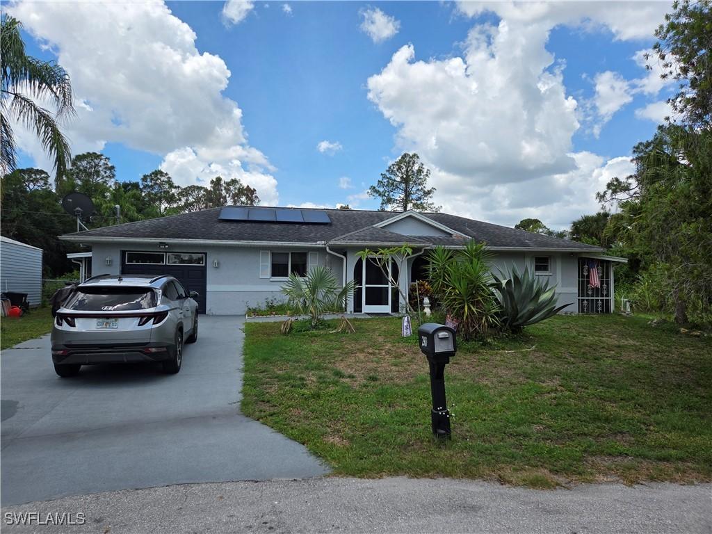 2907 Ashburn St, Lehigh Acres, FL 33972 - single story home with driveway, an attached garage, a front lawn, solar panels, and stucco siding