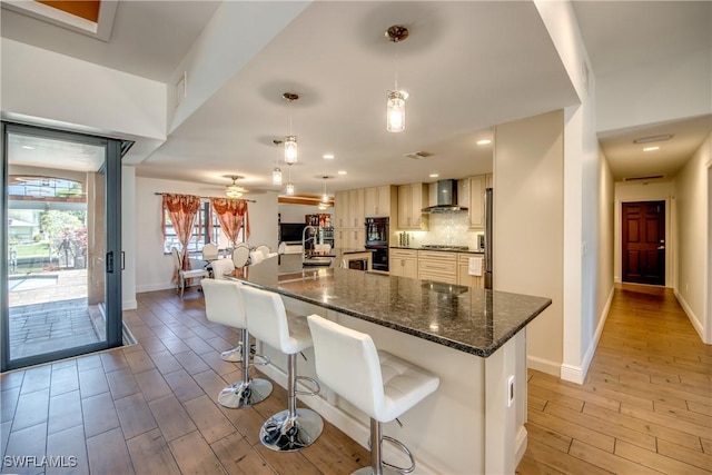 141 SW 39th St, Cape Coral, FL 33914 - kitchen with wall chimney range hood, light wood finished floors, baseboards, cooktop, and a kitchen bar