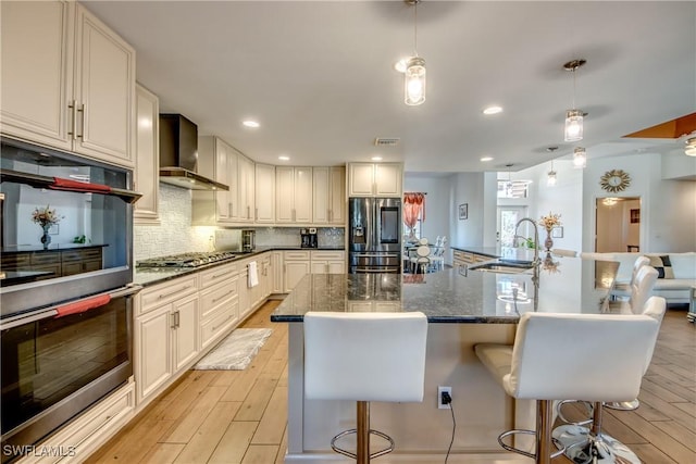 141 SW 39th St, Cape Coral, FL 33914 - kitchen featuring stainless steel appliances, wall chimney exhaust hood, a kitchen bar, light wood finished floors, and recessed lighting