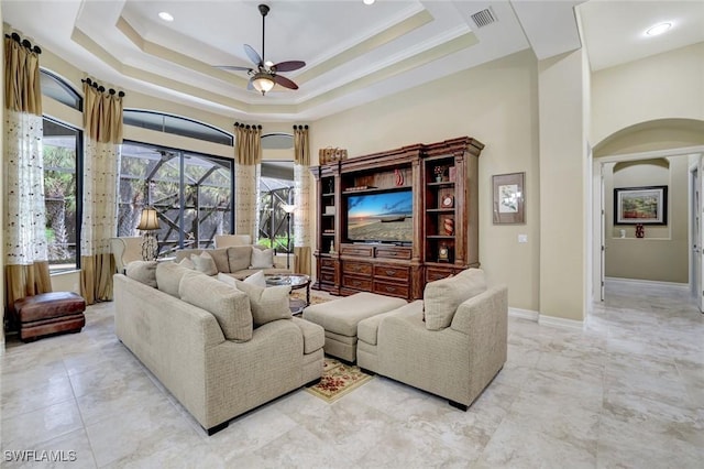 7748 Classics Dr, Naples, FL 34113 - living room with a ceiling fan, arched walkways, a tray ceiling, and baseboards