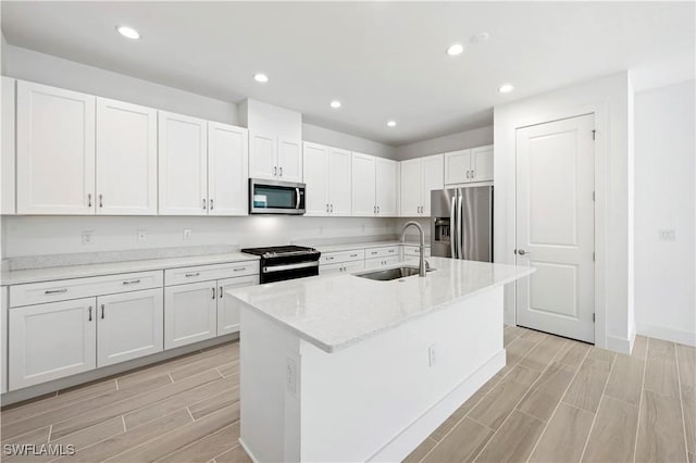 44320 Panther Dr, Punta Gorda, FL 33982 - kitchen with appliances with stainless steel finishes, wood tiled floors, white cabinets, a center island with sink, and light stone countertops