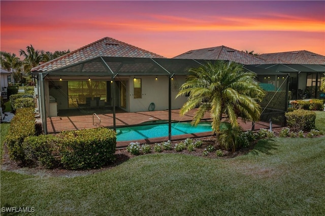 12732 Kinross Ln, Naples, FL 34120 - back of house at dusk with a patio, a lawn, stucco siding, and an outdoor pool