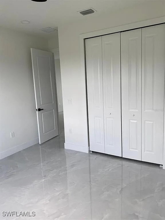 3017 4th St W, Lehigh Acres, FL 33971 - unfurnished bedroom featuring baseboards, marble look tile flooring, and a closet
