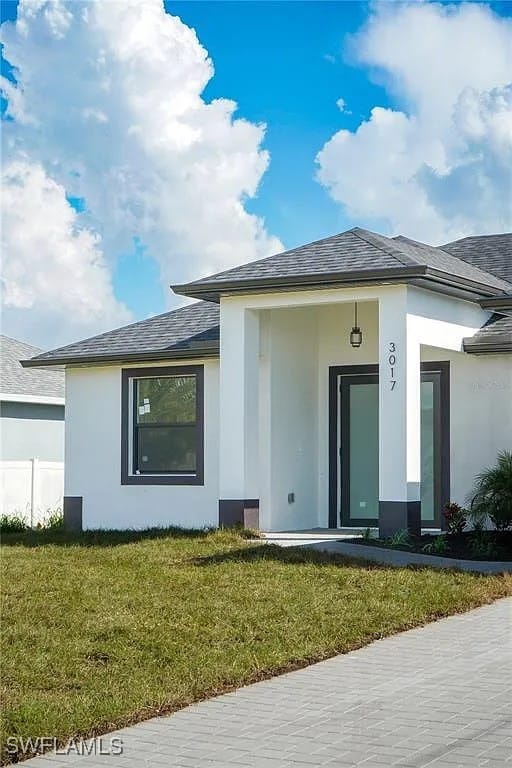 3017 4th St W, Lehigh Acres, FL 33971 - rear view of house with stucco siding, a lawn, and a shingled roof