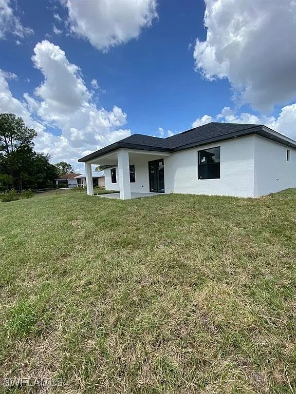 3017 4th St W, Lehigh Acres, FL 33971 - back of property with stucco siding and a yard