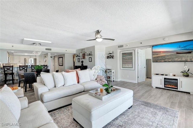 100 N Collier Blvd Unit 1002, Marco Island, FL 34145 - living room featuring a textured ceiling, light wood-type flooring, a glass covered fireplace, ceiling fan, and baseboards