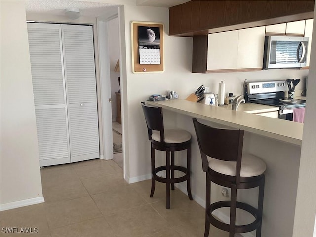 14598 Sagamore Ct, Fort Myers, FL 33908 - kitchen with appliances with stainless steel finishes, a kitchen breakfast bar, light countertops, and light tile patterned flooring